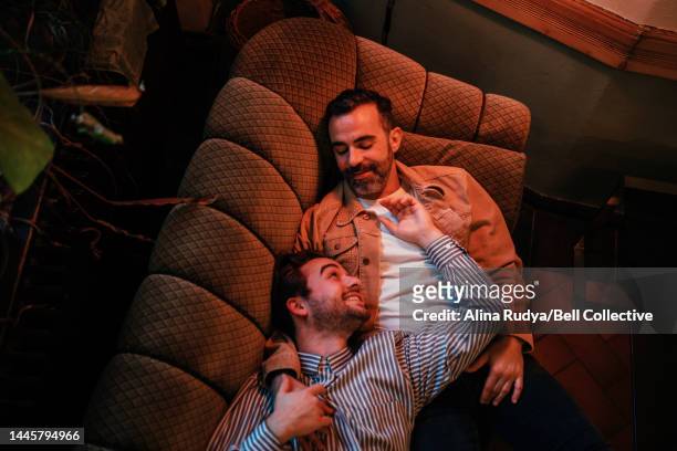 gay couple lying on a couch - freundschaftliche verbundenheit stock-fotos und bilder