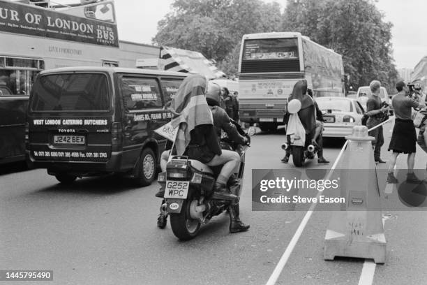 Four people, one wearing a rainbow flag, on motorcycles at the Lesbian and Gay Pride event, London, 24th June 1995.