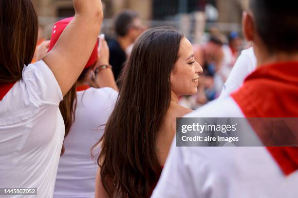 back view of woman standing in the street smiling in the middle of a group of people wearing traditional san fermines clothing - fiesta of san fermin stock pictures, royalty-free photos & images