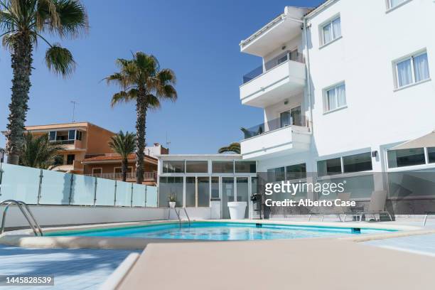 exterior of a mediterranean hotel with swimming pool and sunbeds, perfect for sunbathing on a sunny day - poolside stock pictures, royalty-free photos & images