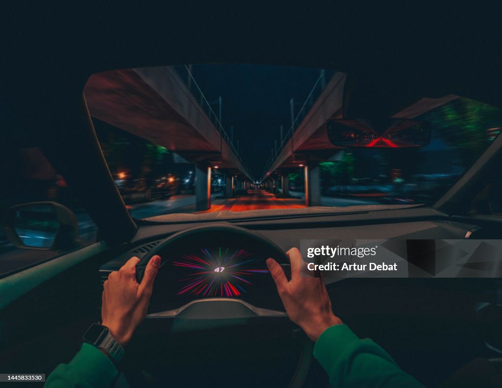 Driving an electric car at night in stunning urban scenario with dramatic effect. POV.