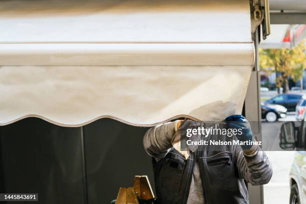 man repairing a white canvas awning - striped awning stock pictures, royalty-free photos & images