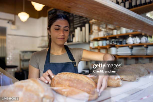 frau, die in einer bäckerei arbeitet und brotlaibe ins regal stellt - bäcker stock-fotos und bilder
