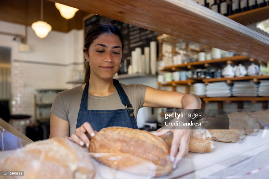 Woman working at a bakery and placing bread loafs on the shelf