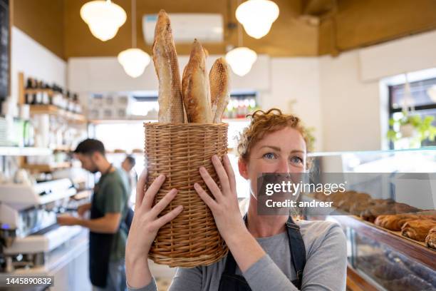 woman working at a bakery and carrying a basket of baguettes - baguette stock pictures, royalty-free photos & images