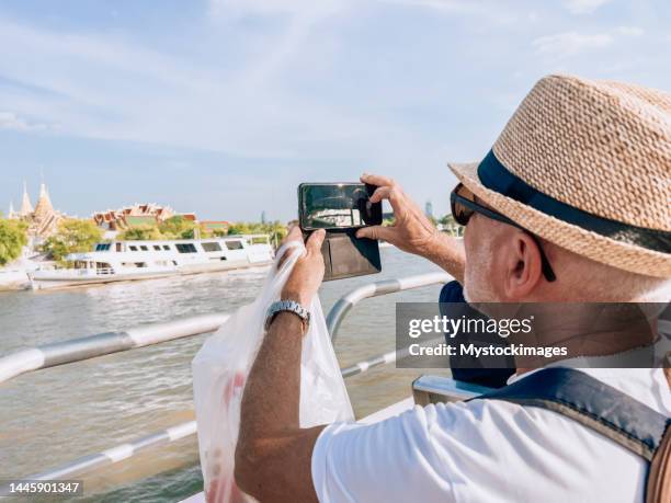 senior man on a ferry trip in bangkok city using mobile phone - river cruise stock pictures, royalty-free photos & images