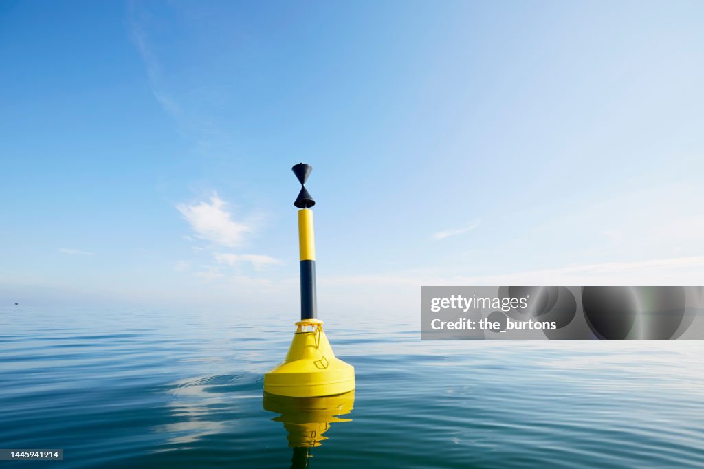 Black yellow striped buoy in smooth sea against blue sky