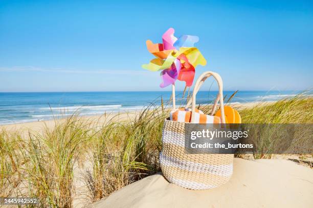 beach bag with colorful pinwheel and towel at sand dunes by the sea - beach bag stock-fotos und bilder