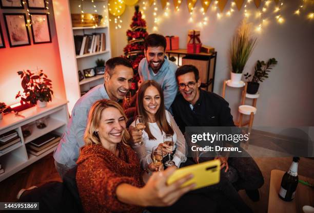 group of diverse friends and family enjoying christmas dinner at home, using smart phone to take selfie - family and happiness and diverse imagens e fotografias de stock