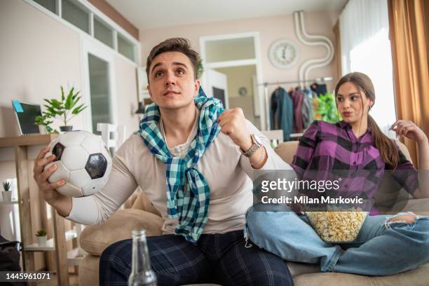 a young couple is watching a sports match, a football game and cheering at home - dating game stock pictures, royalty-free photos & images
