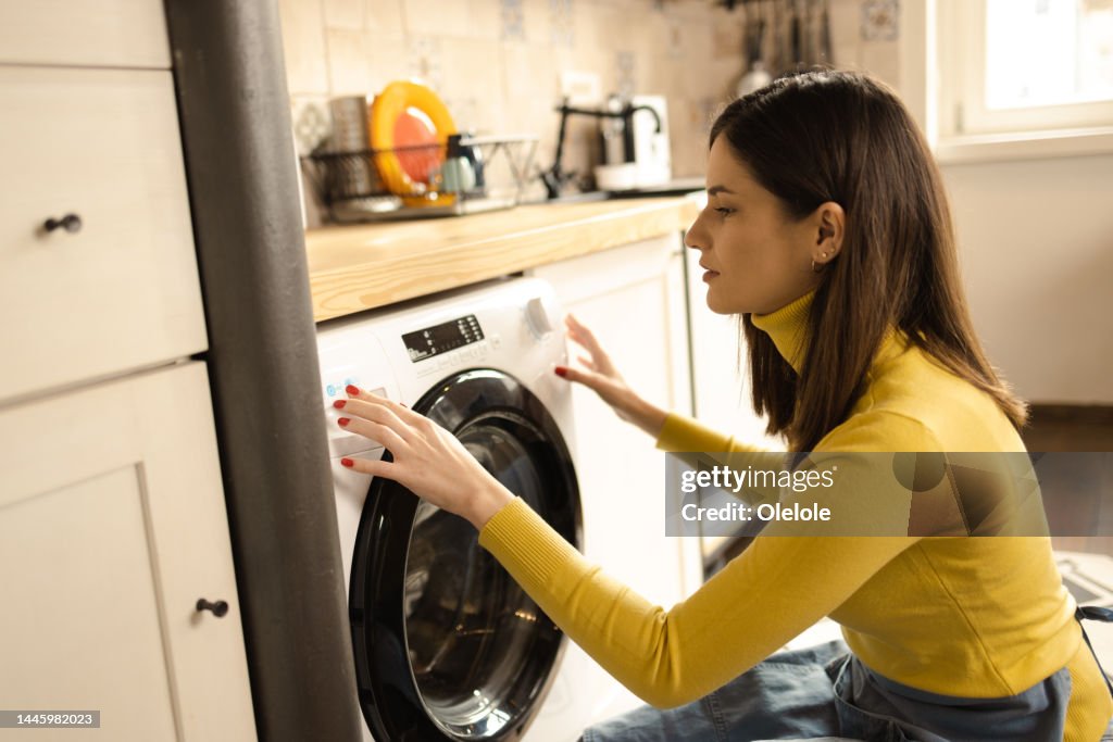 Glückliche junge Frau, die eine Waschmaschine in ihrem Haus einstellt