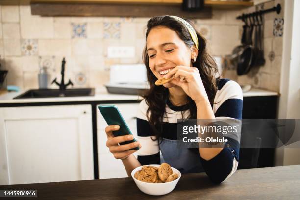 porträt eines schönen mädchens, das online spaß hat, während es kekse nascht - eating cookies stock-fotos und bilder