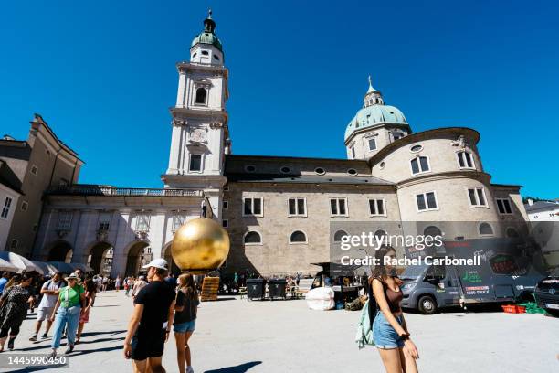 people walking and visiting kapitelplatz with sphaera sculpture and salzburg cathedral at back. - salzburgo stock-fotos und bilder