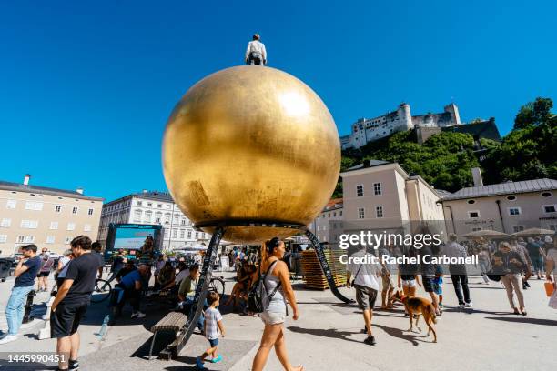 people playing chess, sitting and walking by kapitelplatz square with the sphaera sculpture on the right and hohensalzburg fortress on top of the mountain. - salzburgo stock-fotos und bilder