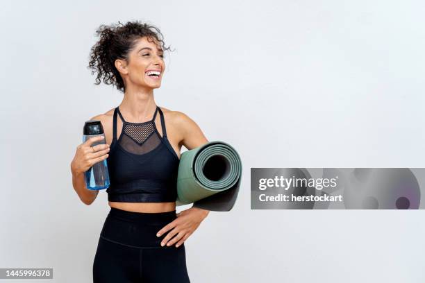 femme souriante devant un mur blanc avec tapis et bouteille d’eau - fitness photos et images de collection