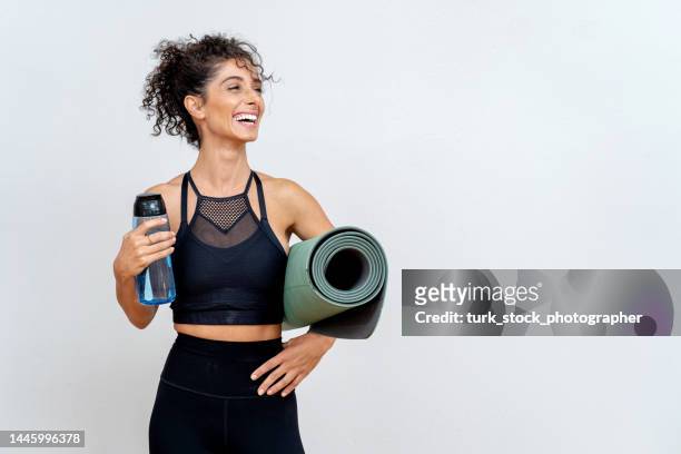 woman smiling in front of white wall with mat and water bottle - träningsmatta bildbanksfoton och bilder