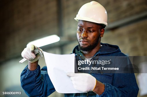 Low-angle View of Male African American industrial worker reading a vernier caliper data and compare with standards check sheet to measure a metal parts after welds process in a factory.