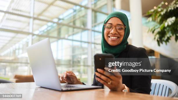 young muslim businesswoman smiling at a text while working on a laptop - muslim head covering stock pictures, royalty-free photos & images