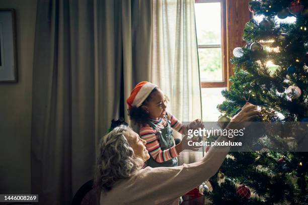 family, christmas tree and decor with a mature woman and child preparing for festive season with love. grandmother, granddaughter and decorating an xmas tree with ornaments and bauble in family home - kerstboom versieren stockfoto's en -beelden
