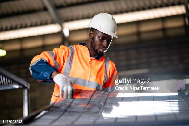 structural steelworks and metal fabrication inspection. low-angle view of a male african american industrial worker holding a metal grate to inspect the quality of the welding process in a metal workshop. - steel worker stock pictures, royalty-free photos & images