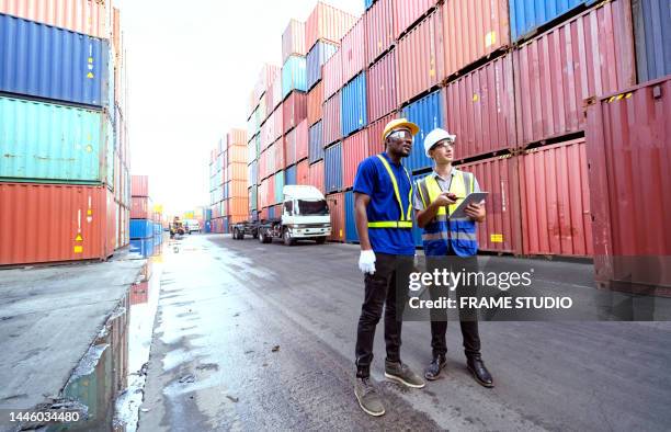 black and white workers or engineers or port workers working together as a teamwork sorting containers or cargo containers, which come from ships, are layered into patterns and transported to the destination as freight transportation by working together a - docklands studio stock pictures, royalty-free photos & images
