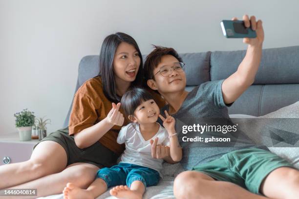 happy family with daughter taking selfie in bed with smartphone - chinese family taking photo at home stock pictures, royalty-free photos & images