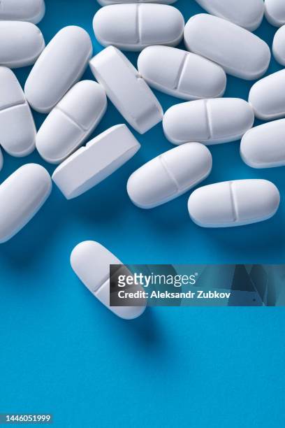 white capsules and tablets on a blue background. taking vitamins, painkillers, medications, and dietary supplements. the concept of pharmaceuticals, prevention and treatment of diseases, healthcare and medicine. pregnancy planning, filling the deficit. - medicamento antiviral imagens e fotografias de stock