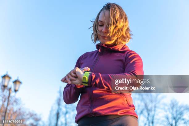 examining of heart rate in park. mature woman in red sportswear check smartwatch application for healthcare in the morning - saturday morning stock pictures, royalty-free photos & images