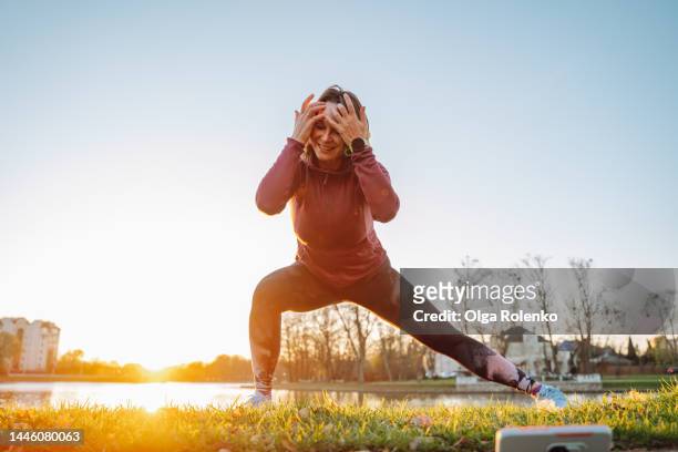 morning workout vlogging using modern technology. mature woman in sports suit warming up before jogging - woman stretching sunset stock-fotos und bilder
