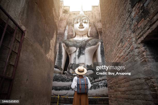 rear view of tourist woman standing in front of huge buddha statue in wat si chum temple located in the north zone of the sukhothai historical park outside the walled city. - sukhothai stock pictures, royalty-free photos & images