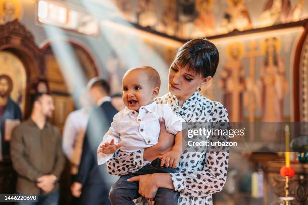 young mother holding her baby during christening in orthodox church - dopen stockfoto's en -beelden