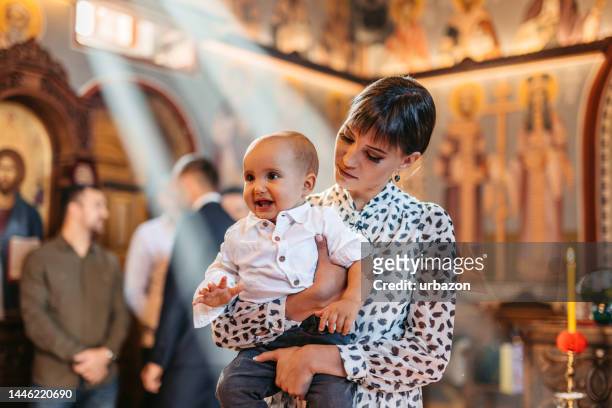 young mother holding her baby during christening in orthodox church - priest baptism stock pictures, royalty-free photos & images