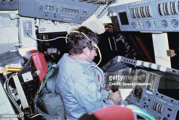 American astronaut John Young logging flight data in a loose-leaf flight activities notebook, sitting at the commander's station on the port side of...