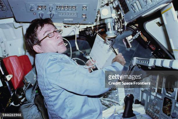 American astronaut John Young prepares to log flight data in a loose-leaf flight activities notebook, sitting at the commander's station on the port...