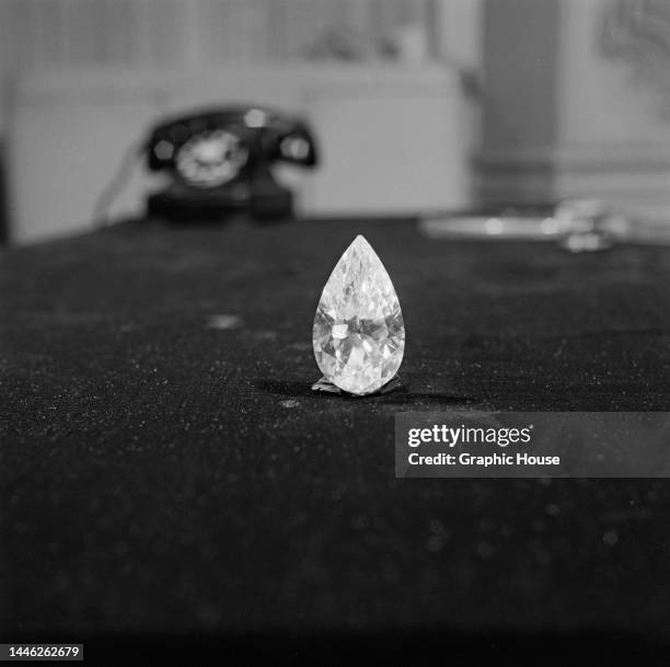 Large pear-shaped diamond balanced in an upright position on a table, with a telephone visible in the background, United States, circa 1950.