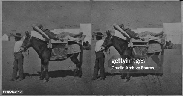 Stereoscopic image showing a man leading a mule carrying a man wounded in an engagement of the Modoc War, tents of a military camp in the background,...