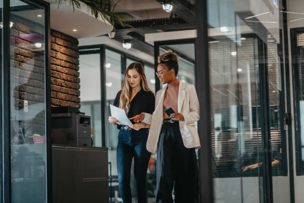 young female employees walking down the company corridor - modern stock pictures, royalty-free photos & images