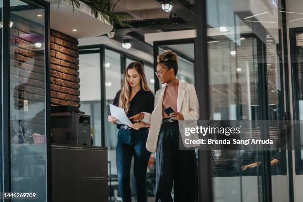young female employees walking down the company corridor - people talking in office corridor stock pictures, royalty-free photos & images
