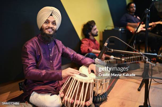 young sikh man smiling and playing tabla and looking at the camera - sitar stockfoto's en -beelden