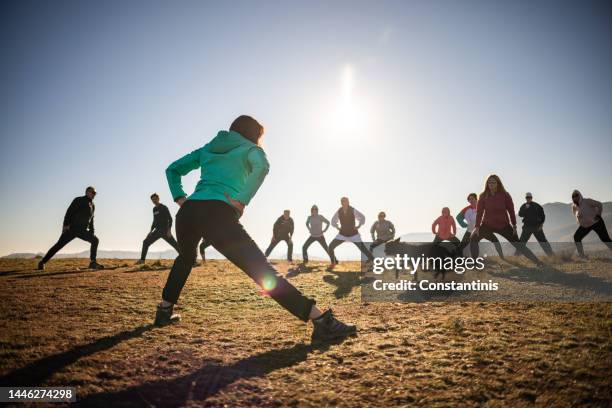 en la naturaleza, grupo de personas caucásicas, estírese, durante la clase de gimnasia grupal dirigida por un instructor - practicing fotografías e imágenes de stock