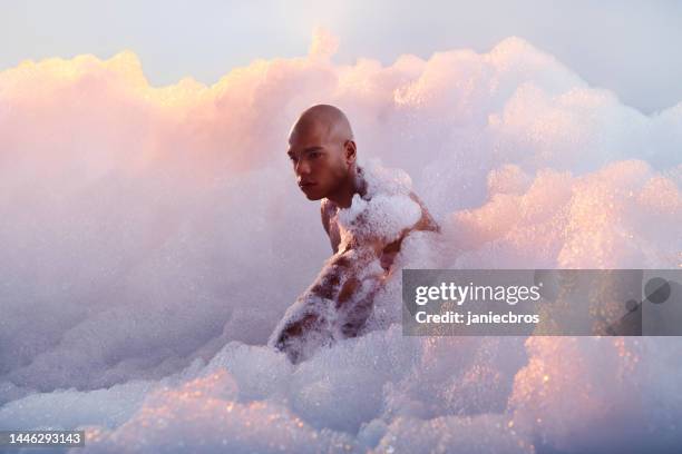 hübscher afrikanischer ethnizitätsmuskulöser mann, der sich auf einer blasenwolke entspannt. selbstpflege und wellness-metapher. vertikales bild - badezimmer mann stock-fotos und bilder