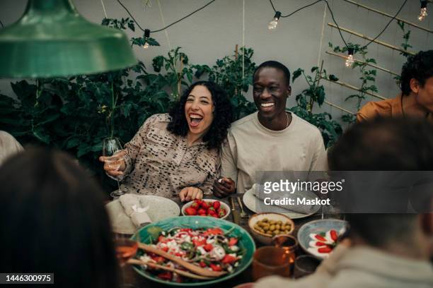Cheerful female and male friends enjoying dinner party in garden during sunset
