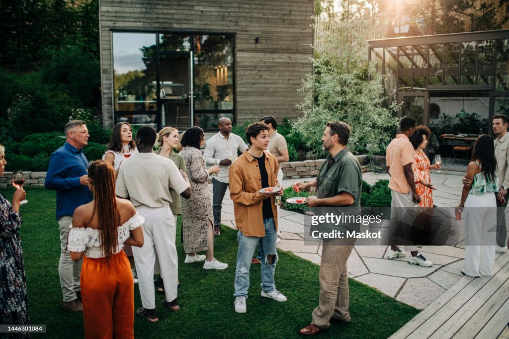 Multiracial male and female colleagues having dinner during garden party