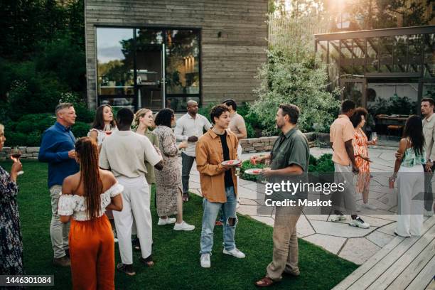 multiracial male and female colleagues having dinner during garden party - social gathering stock pictures, royalty-free photos & images