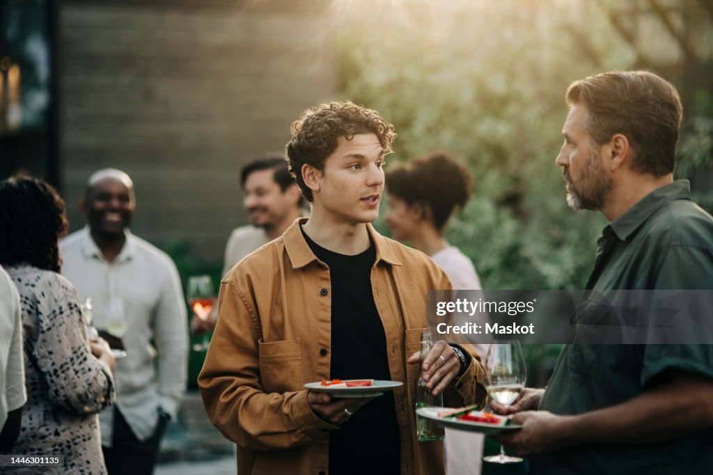 Male colleagues discussing during dinner party in garden at sunset