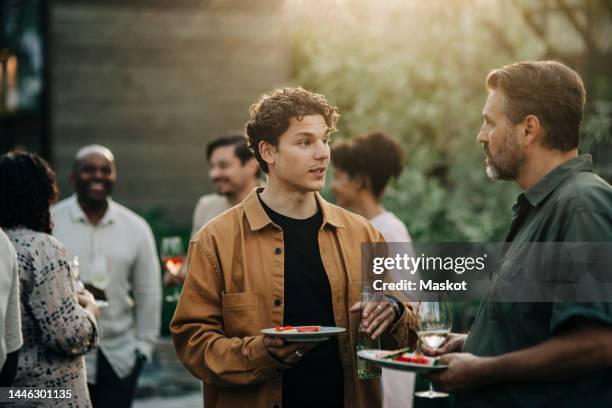 male colleagues discussing during dinner party in garden at sunset - middagsbjudning bildbanksfoton och bilder