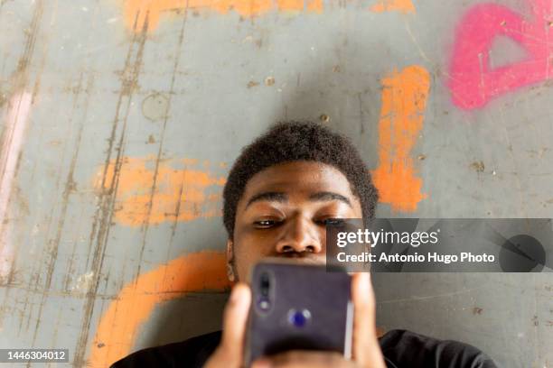 portrait of black boy lying in an abandoned building. surfing with the mobile phone. - sending stock pictures, royalty-free photos & images