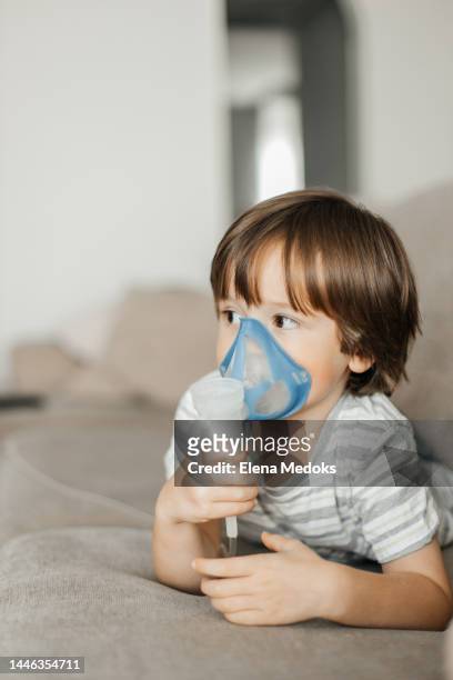 little boy toddler makes inhalation with a nebulizer at home lying on the couch - breath test stockfoto's en -beelden