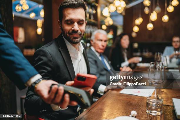 a man is paying the bill at the restaurant using his smart phone - paying for dinner imagens e fotografias de stock