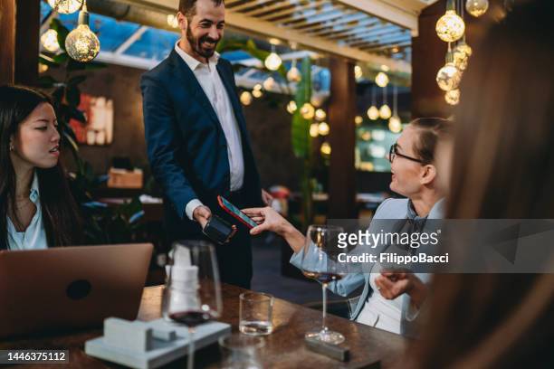 a woman is paying the bill in a luxury restaurant during a meeting with colleagues - paying for dinner imagens e fotografias de stock